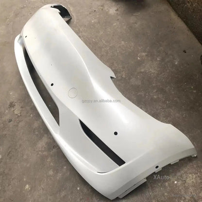 Primed white front bumper cover resting on shop floor, top surface view with openings